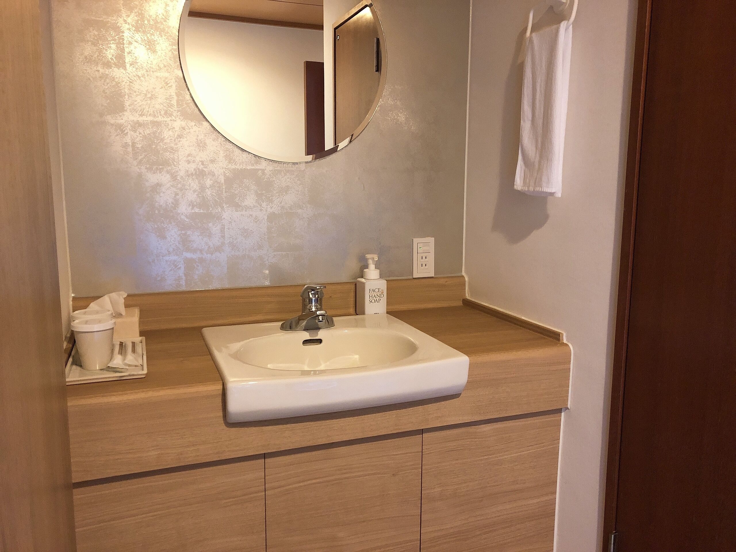 A bathroom with a white sink, a mirror, a soap dispenser, and a towel hanging on the wall.