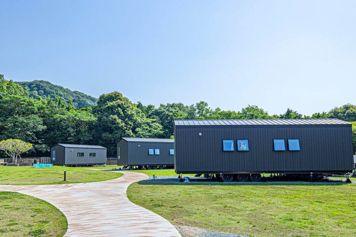 Varias cabañas modulares con un sendero curvo que las conecta, ubicadas en una zona de césped con una colina boscosa al fondo.