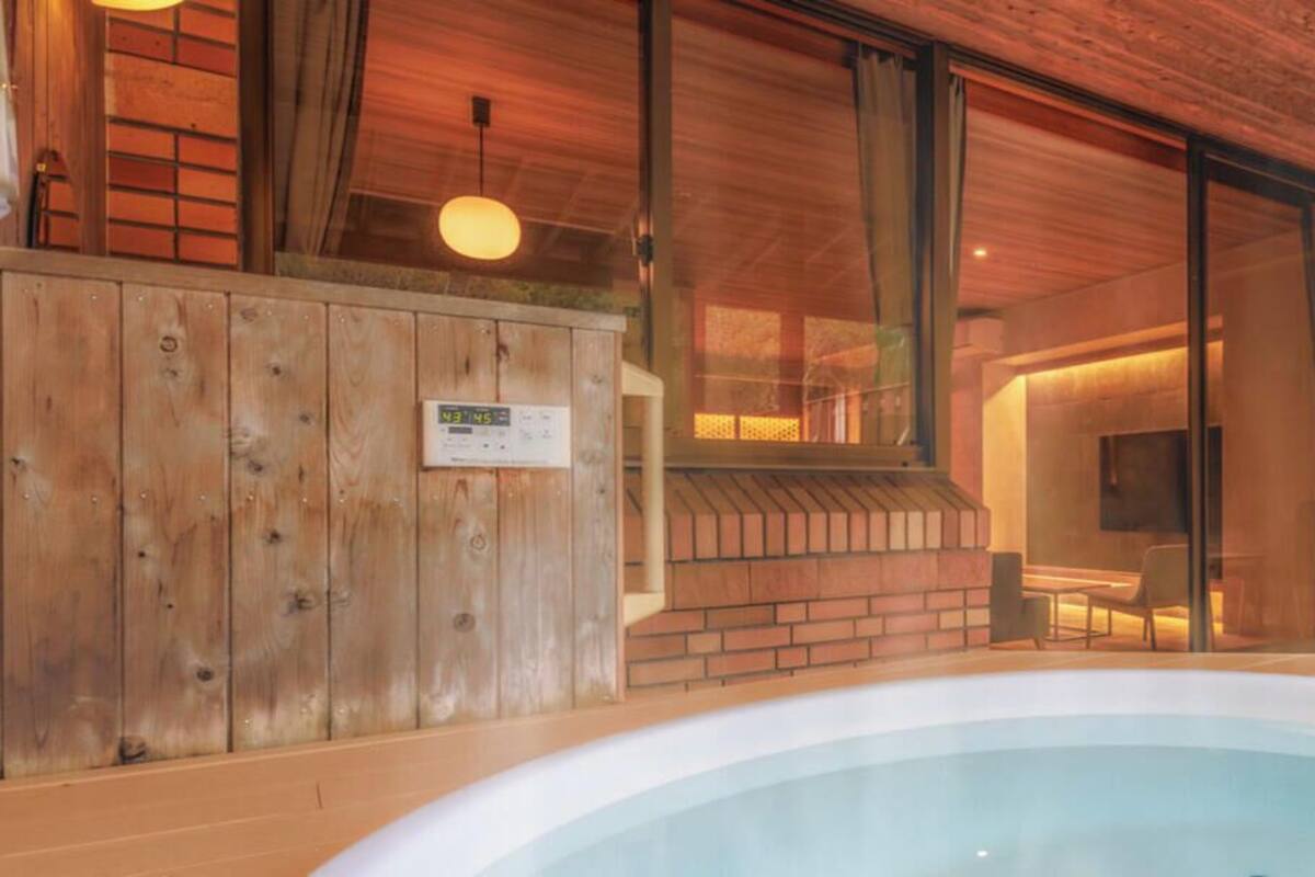Un interior de madera con un jacuzzi, una pared de ladrillo y una puerta de cristal que da a una habitación con televisión.