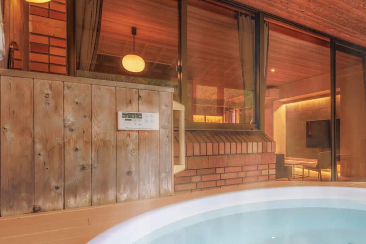 A wooden interior with a hot tub, a brick wall, and a glass door leading to a room with a television.
