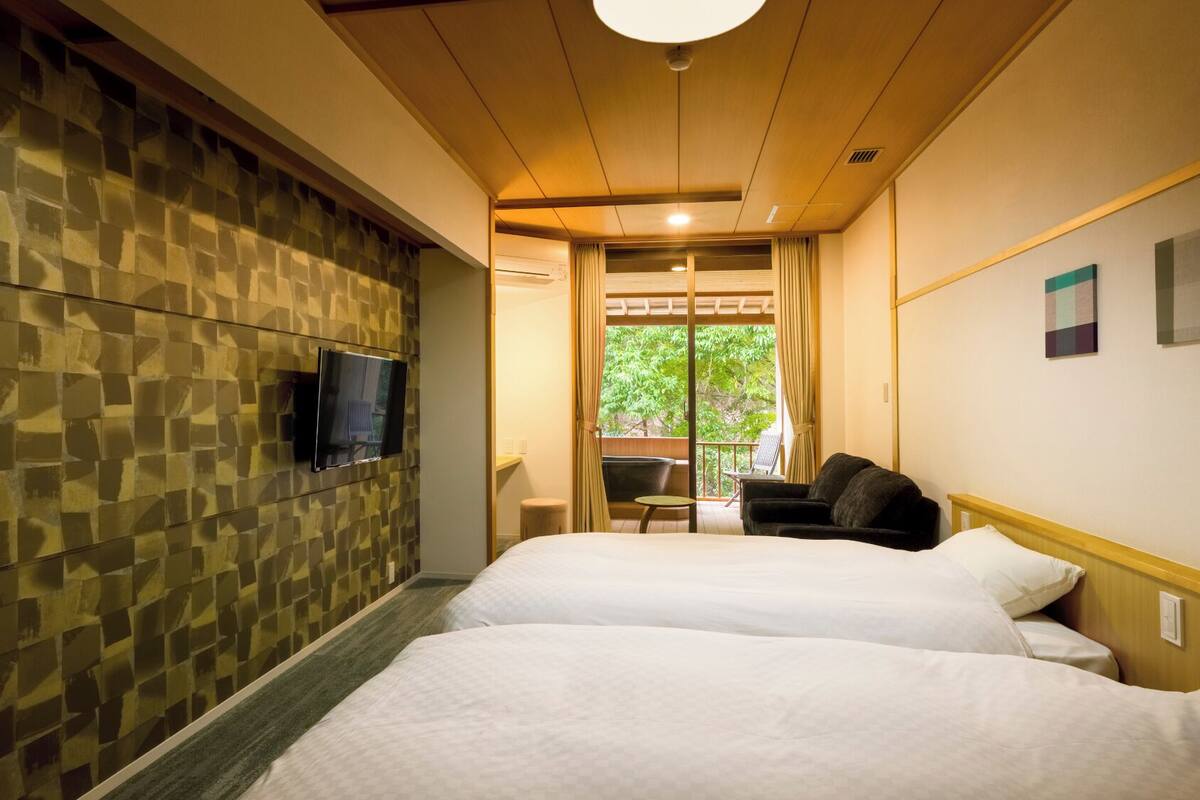 Habitación de hotel con dos camas, un televisor montado en la pared y vista a zonas verdes.