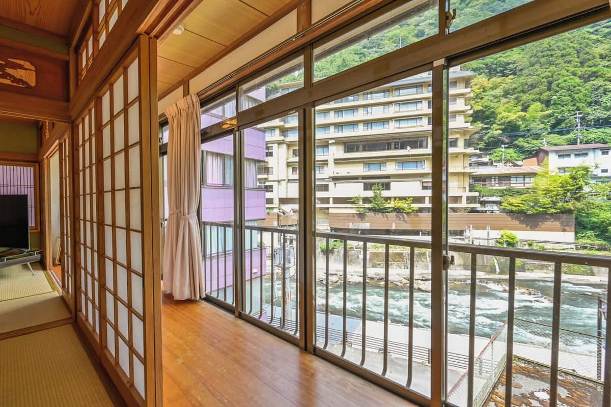 Ein traditioneller japanischer Raum mit Tatami-Böden, einem Fernseher und Blick auf einen Fluss und Gebäude.