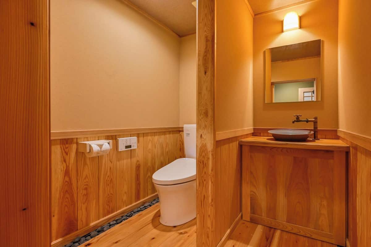 Ein Badezimmer mit Holzverkleidung, einer Toilette, einem Waschbecken mit Spiegel darüber und einem Wandthermostat.