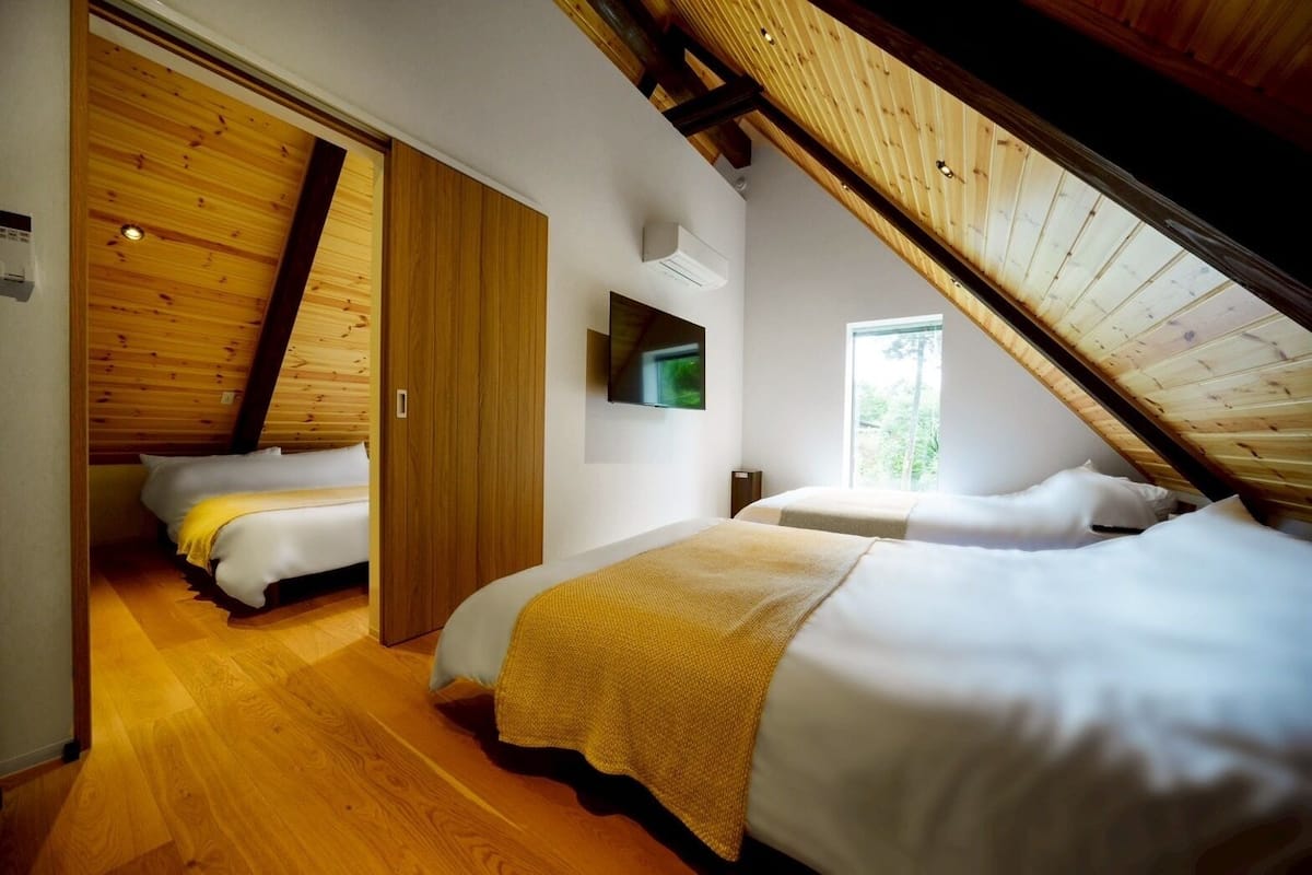 Ein Schlafzimmer mit zwei Betten, Holzboden, einem Fernseher und einem Fenster.