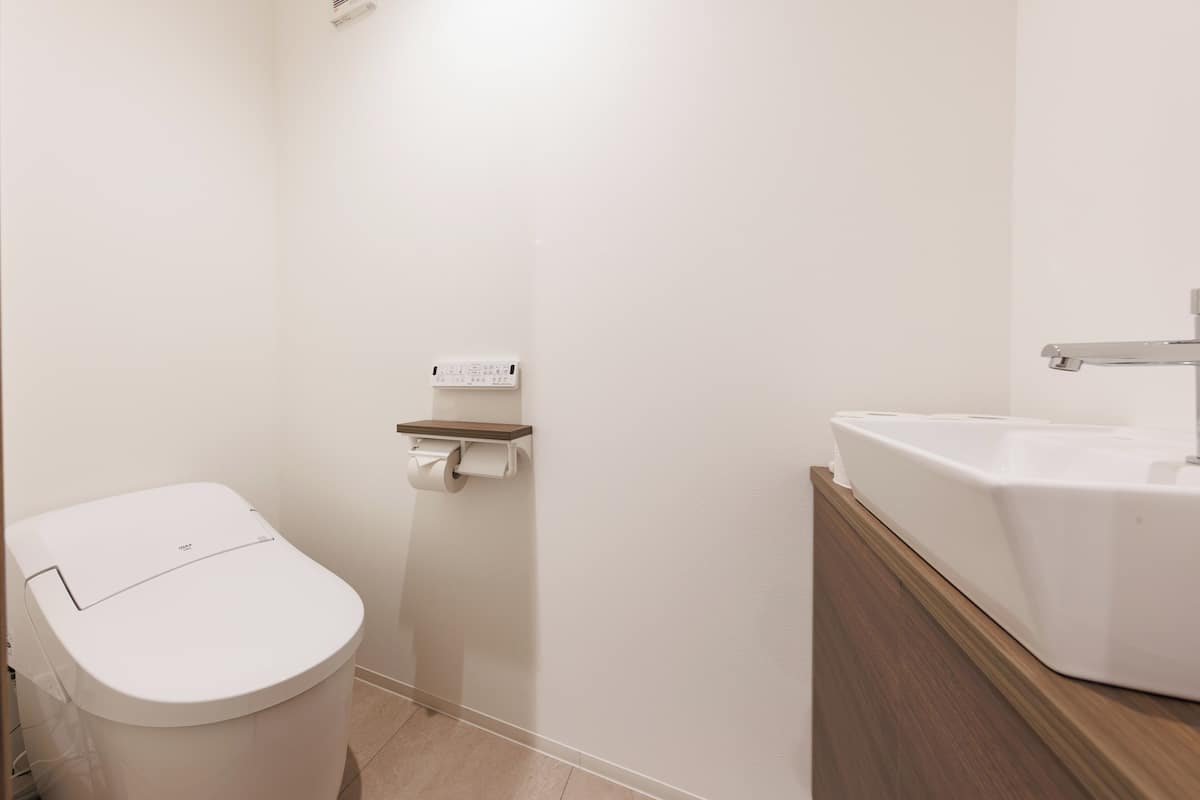 Ein Badezimmer mit Toilette, einem an der Wand befestigten Toilettenpapierhalter und einem Waschbecken mit Holzplatte.