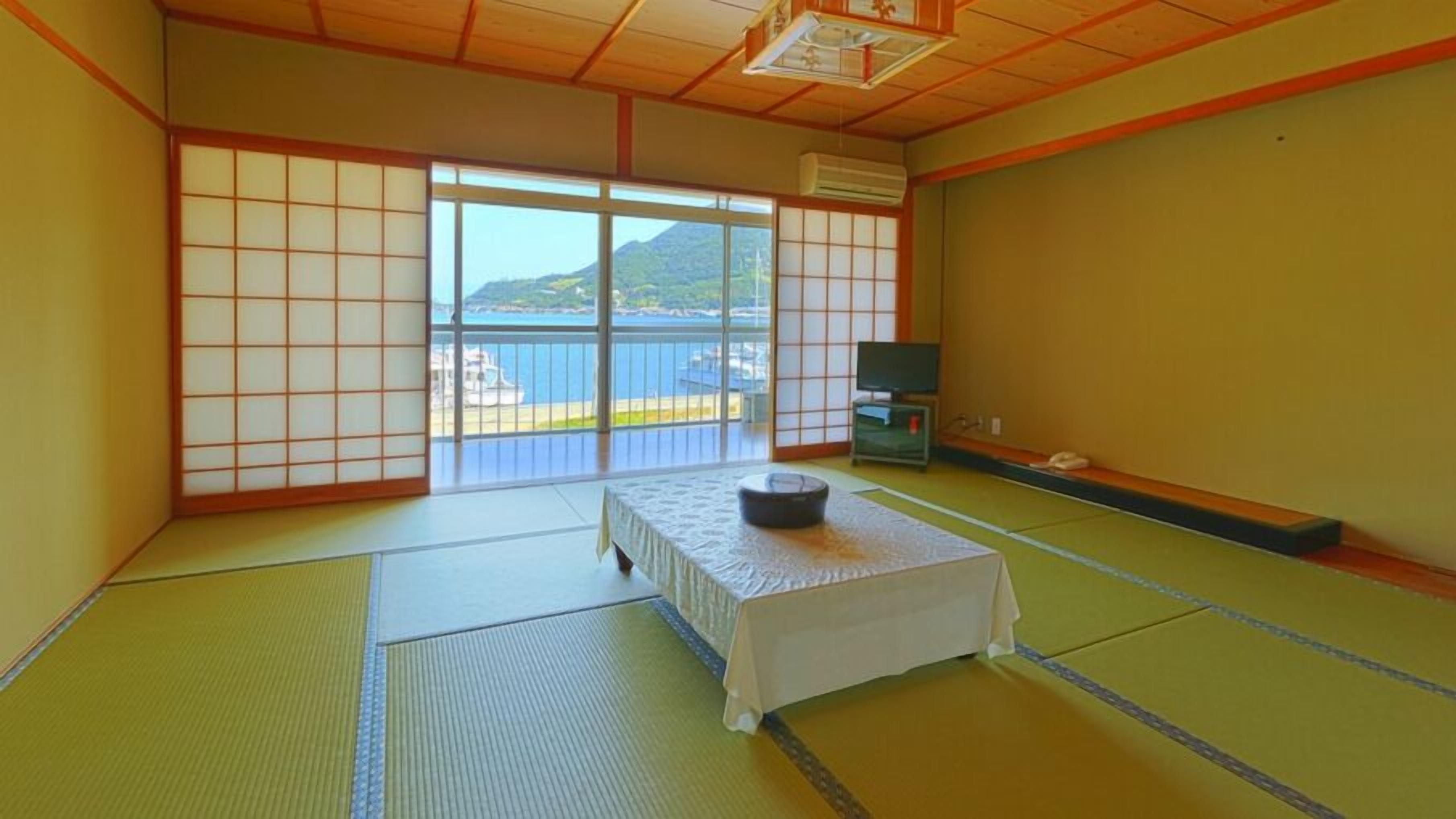 Une pièce de style japonais traditionnel, avec un sol recouvert de tatamis, une table basse en tatami, un futon servant de lit, une télévision et une vue sur la mer.