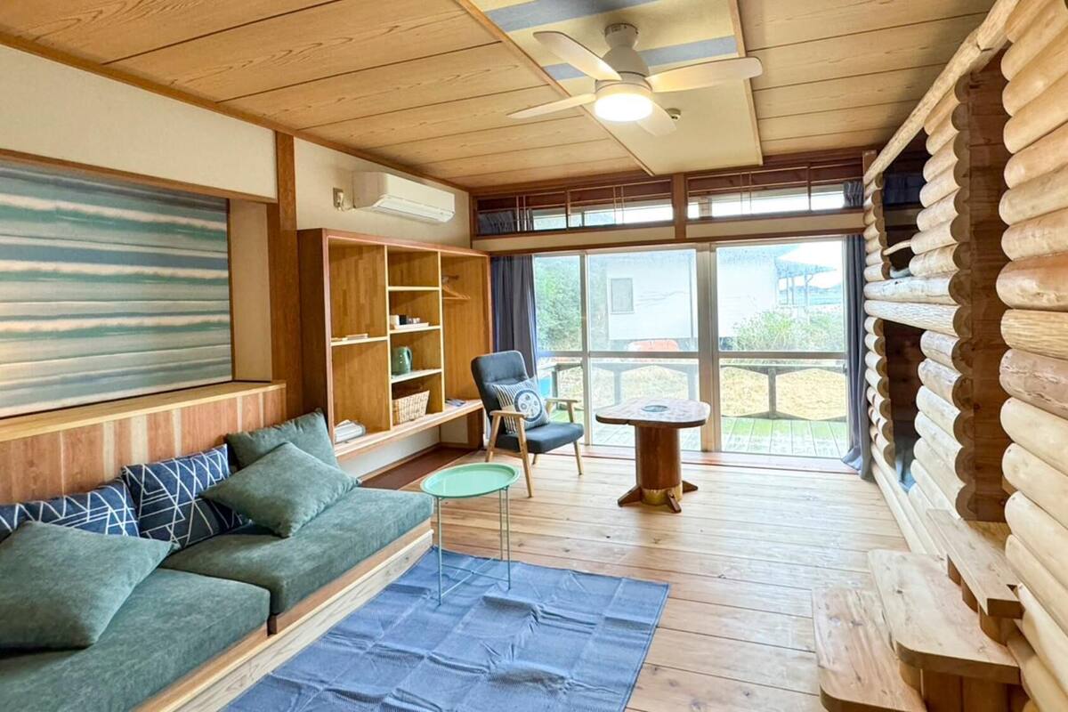 Ein rustikaler Innenraum einer Blockhütte mit einer Couch, einem Sessel, einem kleinen Tisch und einem Bücherregal.
