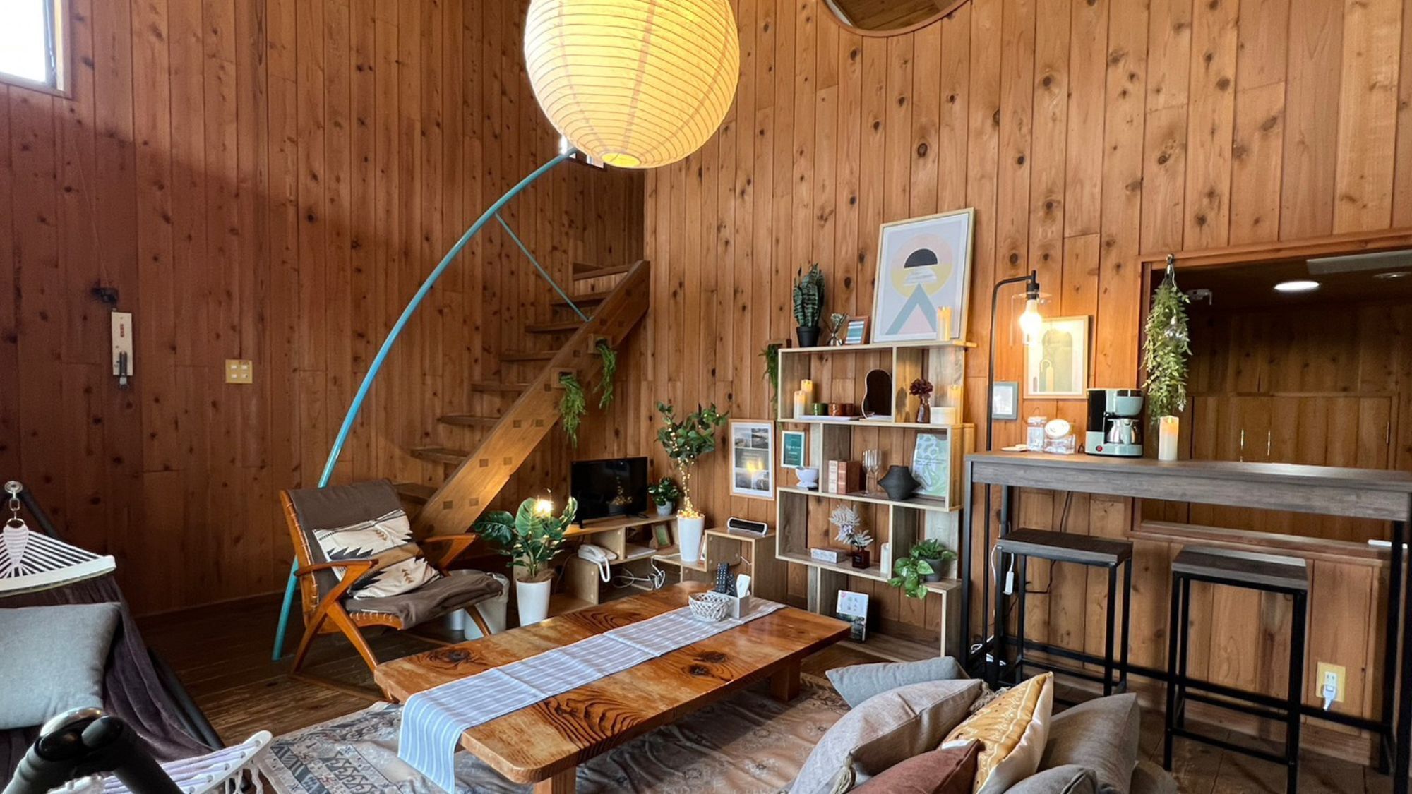 A cozy room with a wooden floor, a wooden bench, a table with a striped tablecloth, a TV, and a bookshelf with various items.