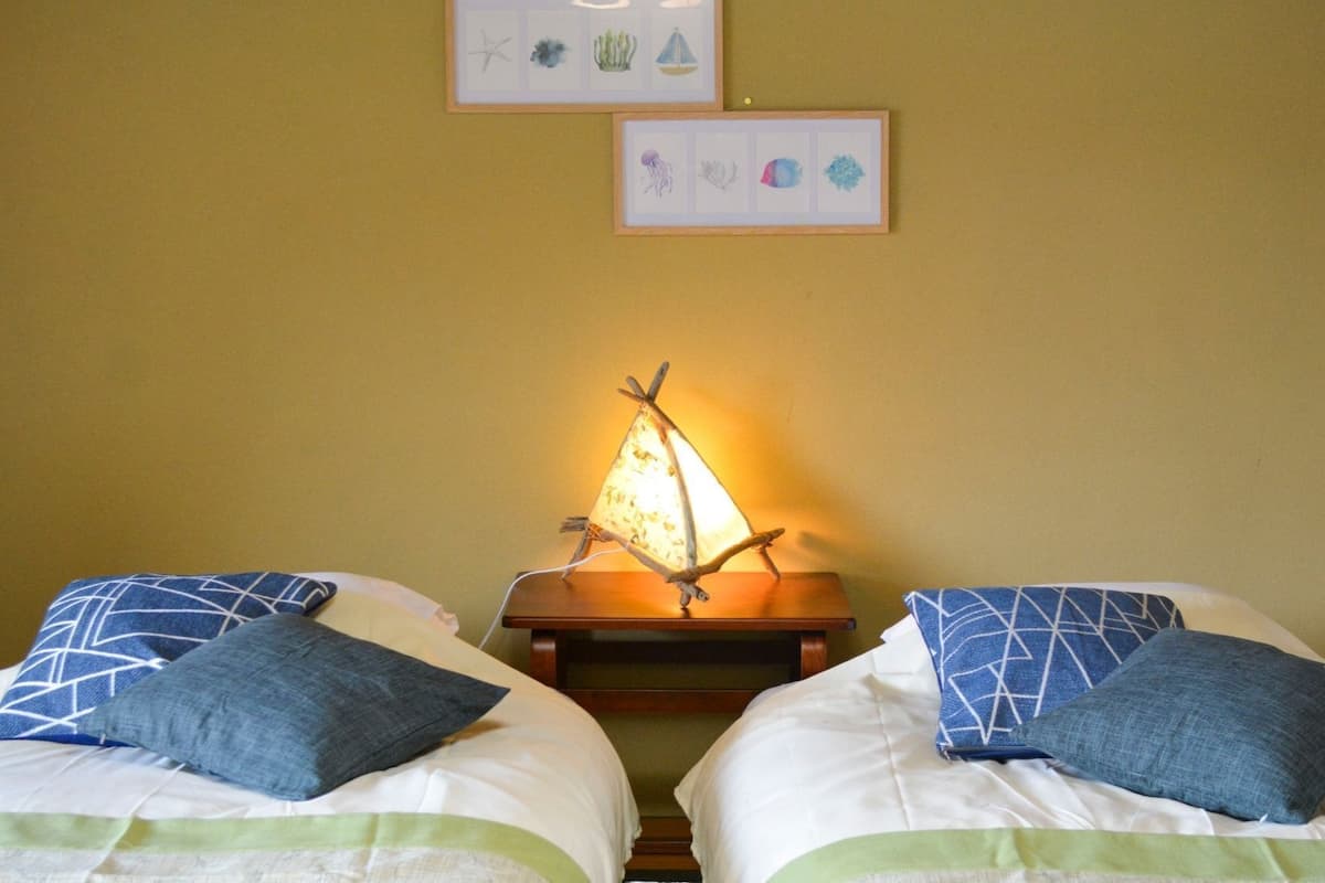 Zwei Betten mit blauen Kissen, eine Wandlampe und zwei gerahmte Bilder darüber.