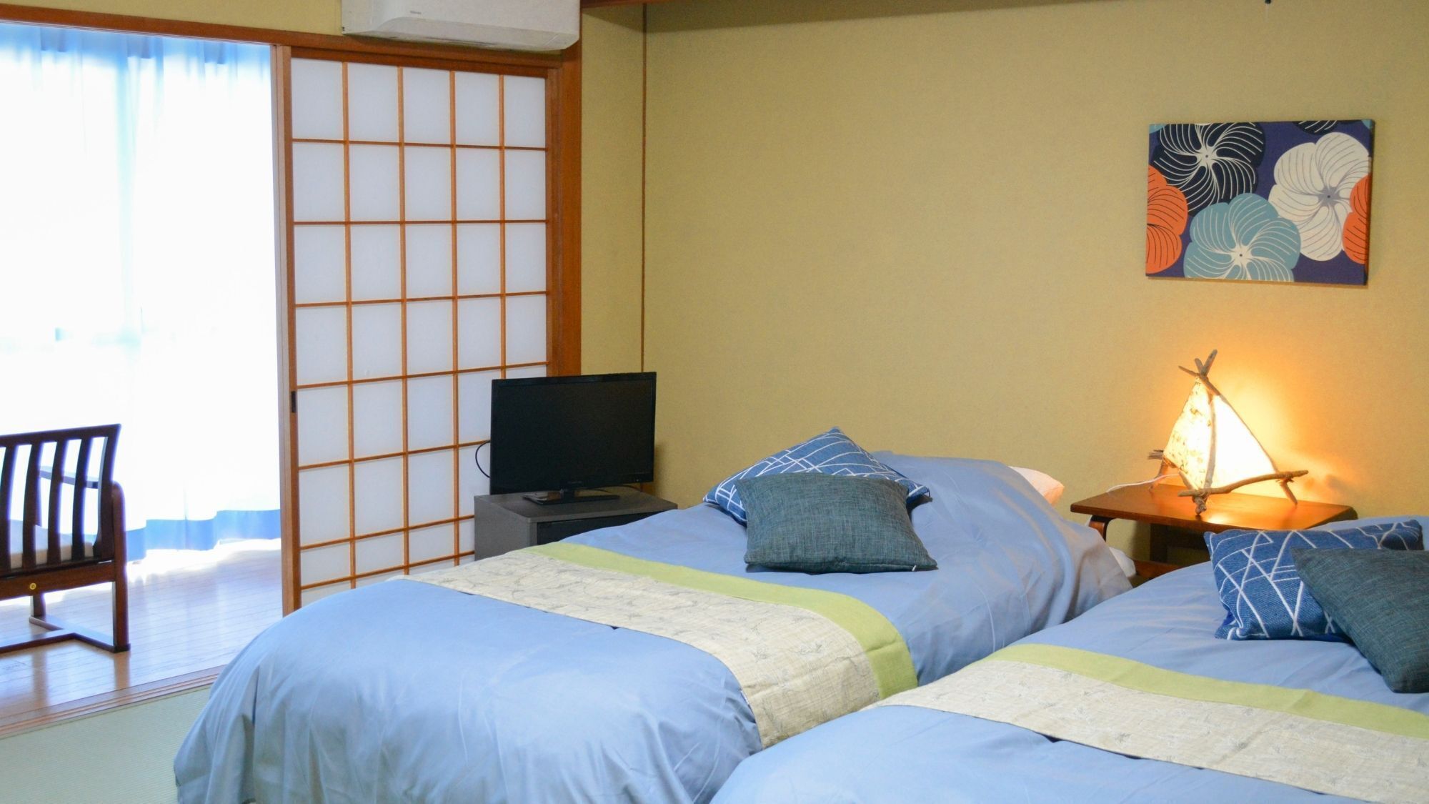 Une chambre d’hôtel avec deux lits, une télévision, un bureau, une chaise et un tableau au mur.