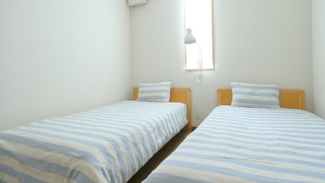 A room with two single beds, a window with a lamp, and a white wall.