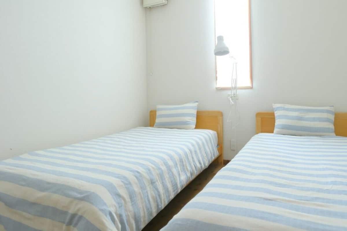 Ein Zimmer mit zwei Einzelbetten, einem Fenster inklusive Lampe und einer weißen Wand.