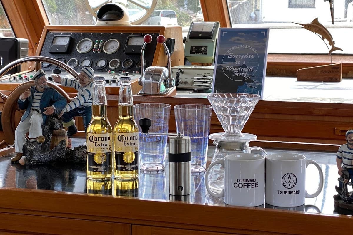 Schiffsrad, Flaschen Corona Extra, Tsuru Maru Kaffeetassen und eine Figur auf einer Holztischplatte.