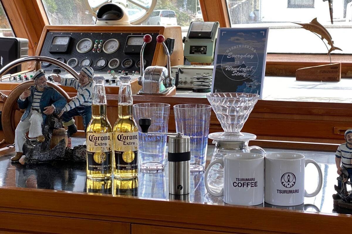 Un gouvernail de navire, des bouteilles de Corona Extra, des tasses à café Tsuru Maru et une figurine sur une surface en bois.