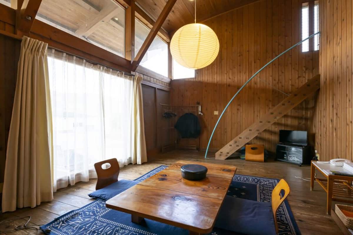 Ein Holzinterieur mit einem Esstisch, Stühlen, einer Hängelampe und einer Treppe.