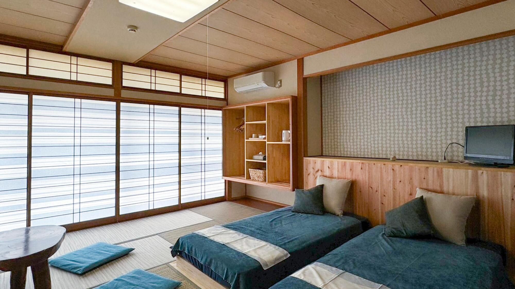Une pièce de style japonais traditionnel, avec un sol recouvert de tatamis, un futon servant de lit, une étagère intégrée avec des rangements, une télévision et une grande fenêtre dotée de panneaux coulissants en papier de riz (shoji).