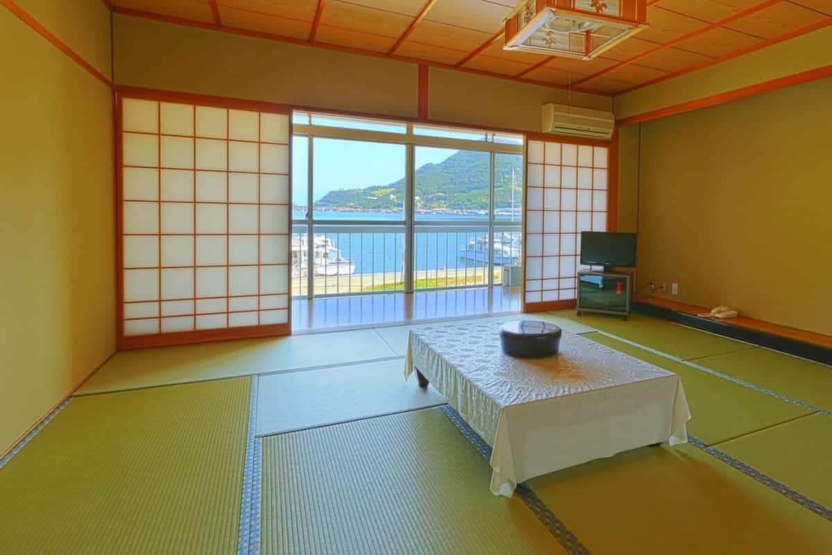 Ein traditioneller japanischer Raum mit Tatami-Bodenbelag, einem Tisch aus Tatami-Matten, einem Fernseher und Blick aufs Meer.