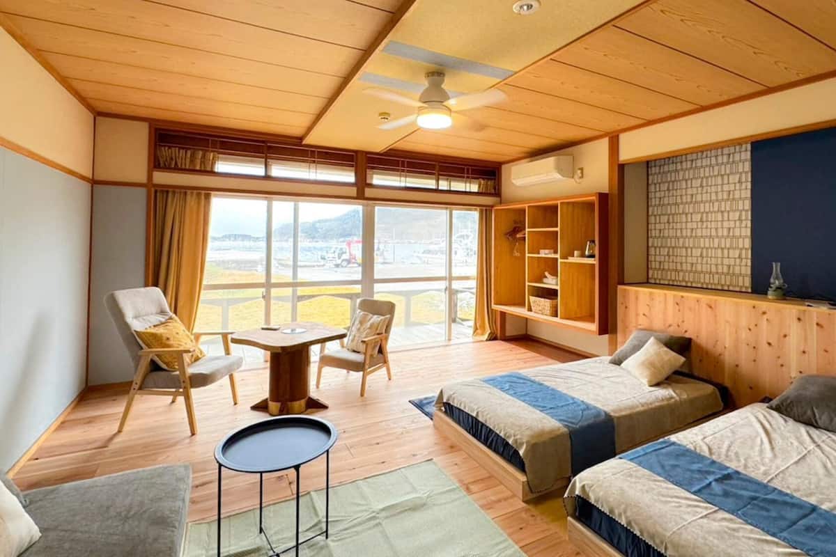 Ein Zimmer mit zwei Betten, einem kleinen Tisch, einem Stuhl, einem Fernseher und einem großen Fenster mit Blick.