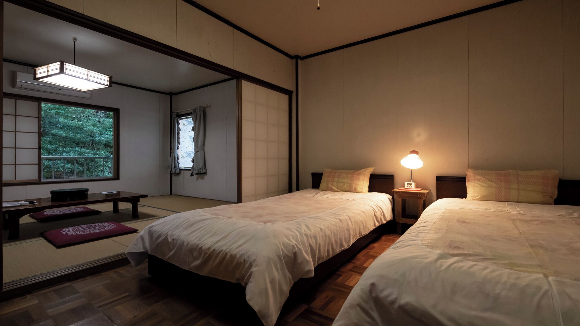 A traditional Japanese-style room with tatami flooring, two beds, a low table, and a sliding door leading to a garden.