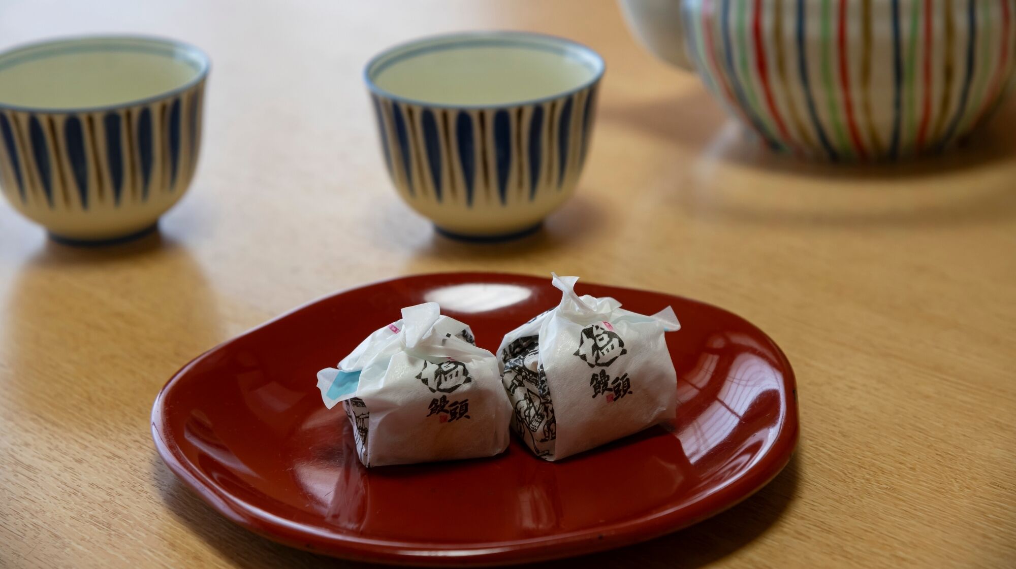 A red plate with two wrapped items on a wooden table.