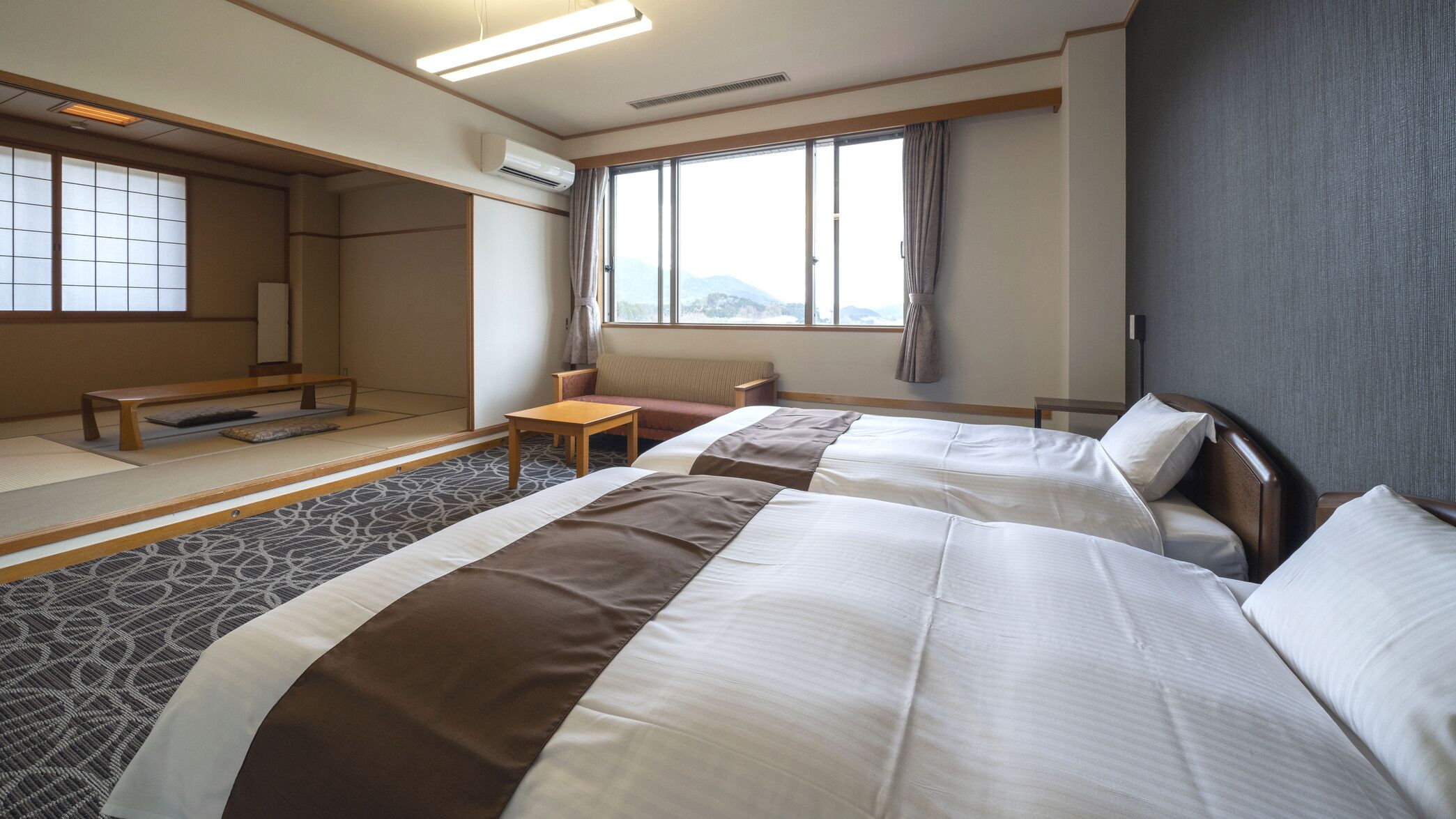 A hotel room with two beds, a sofa, a small table, and a view of the mountains.