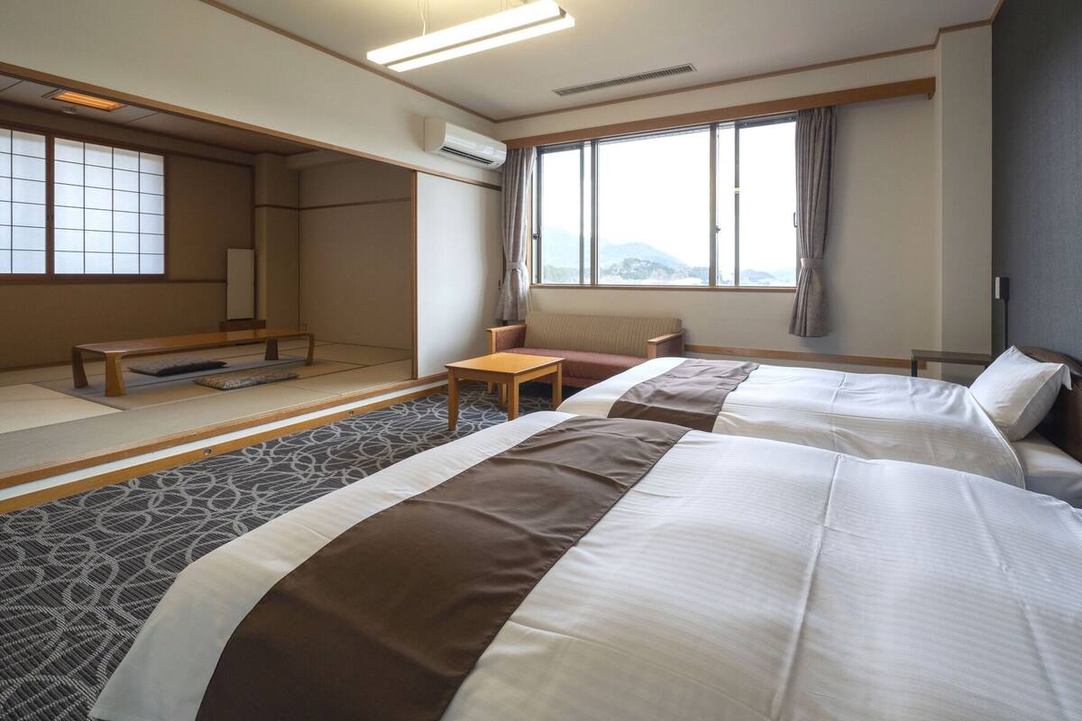 Habitación de hotel con dos camas, un sofá, una mesita y vistas a las montañas.