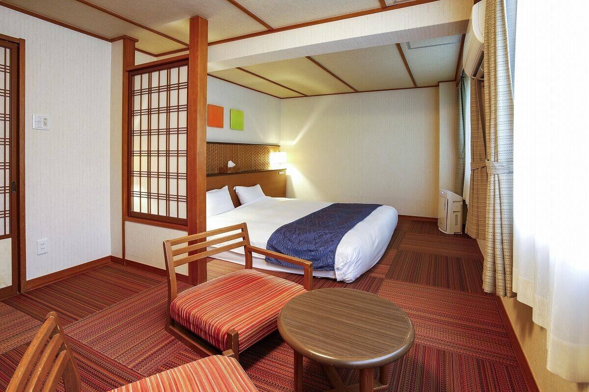 Habitación de hotel con cama, una silla, una mesita, una ventana con cortinas y un panel decorativo en la pared.
