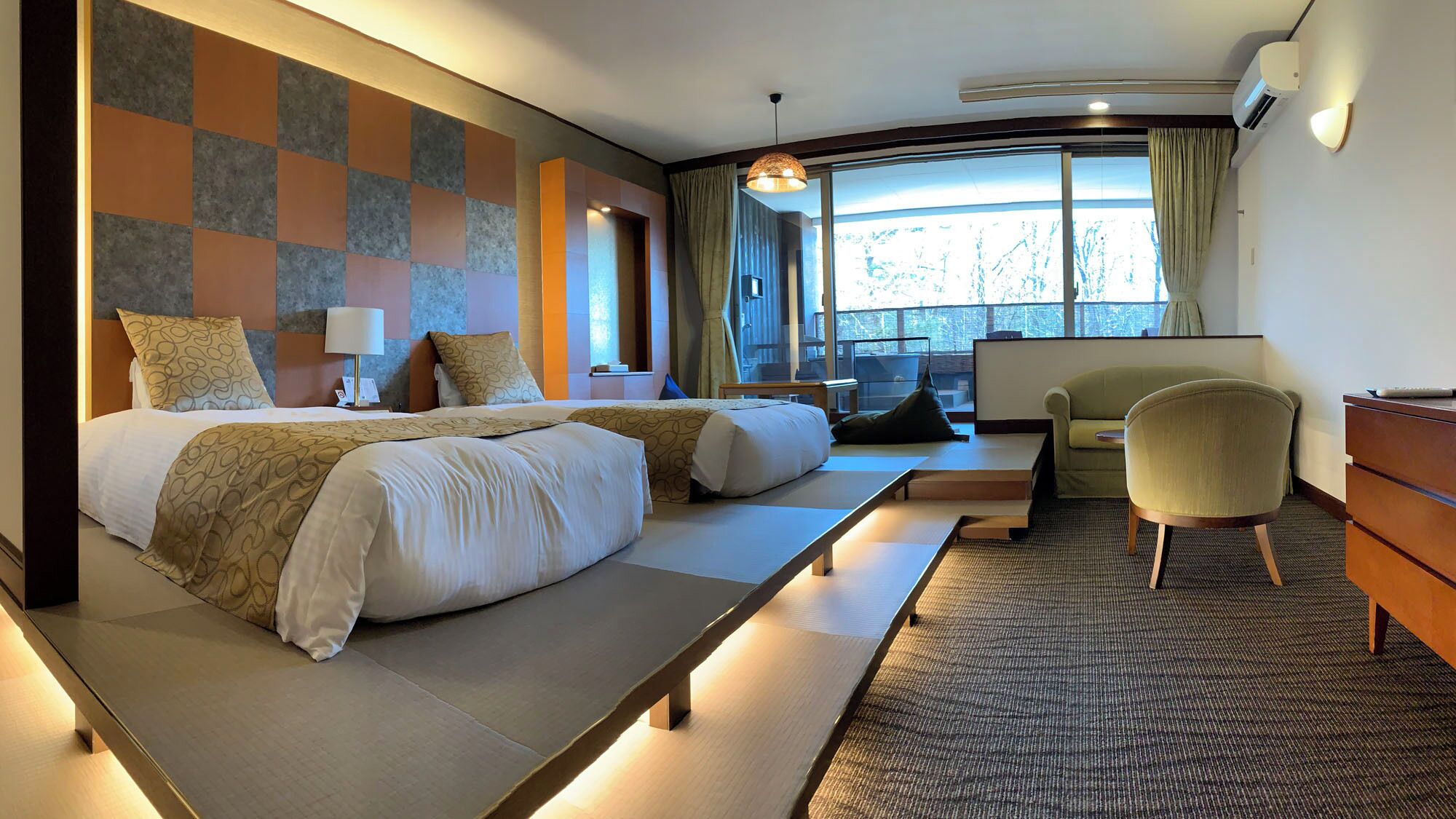 A hotel room with two beds, a desk, a chair, and a large window with curtains.