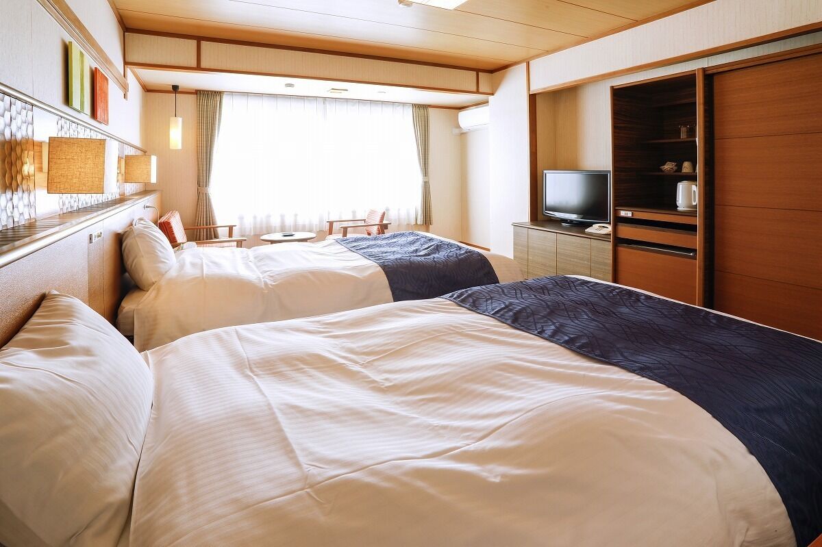 A hotel room with two beds, a television, a small table, and a wardrobe.