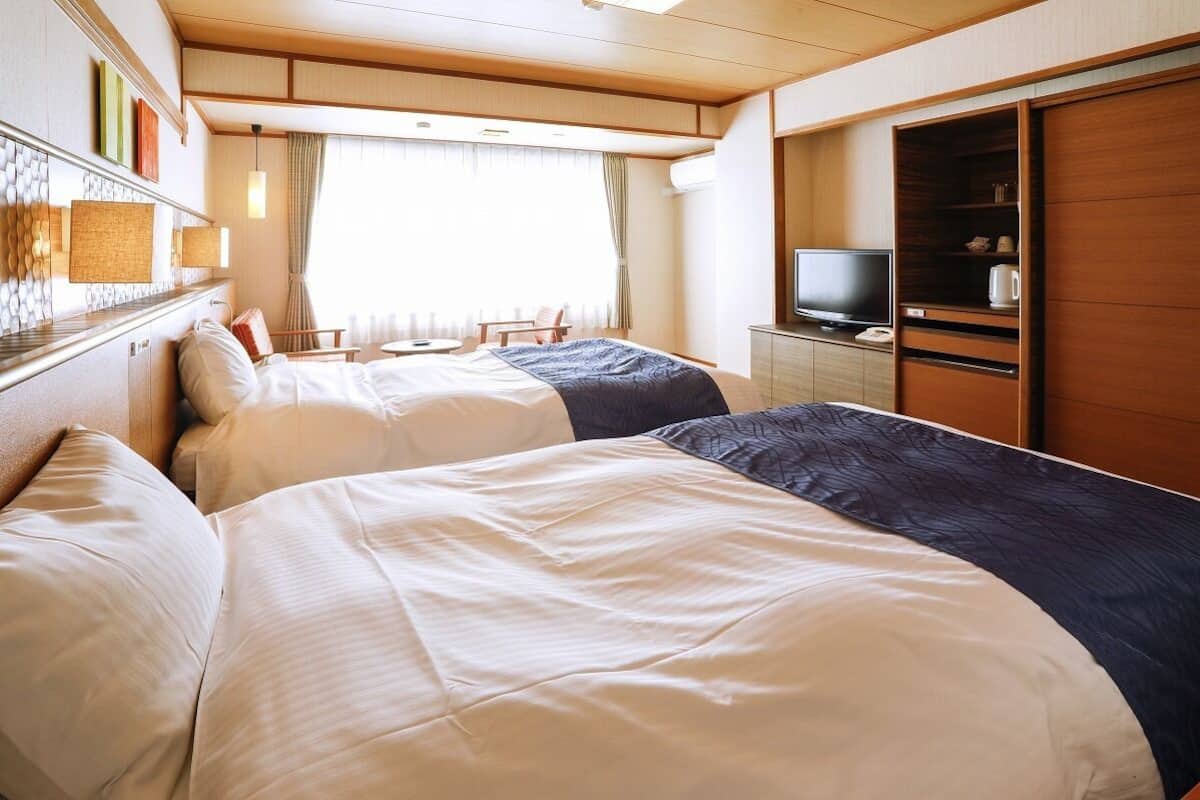 Habitación de hotel con dos camas, un televisor, una mesita y un armario.