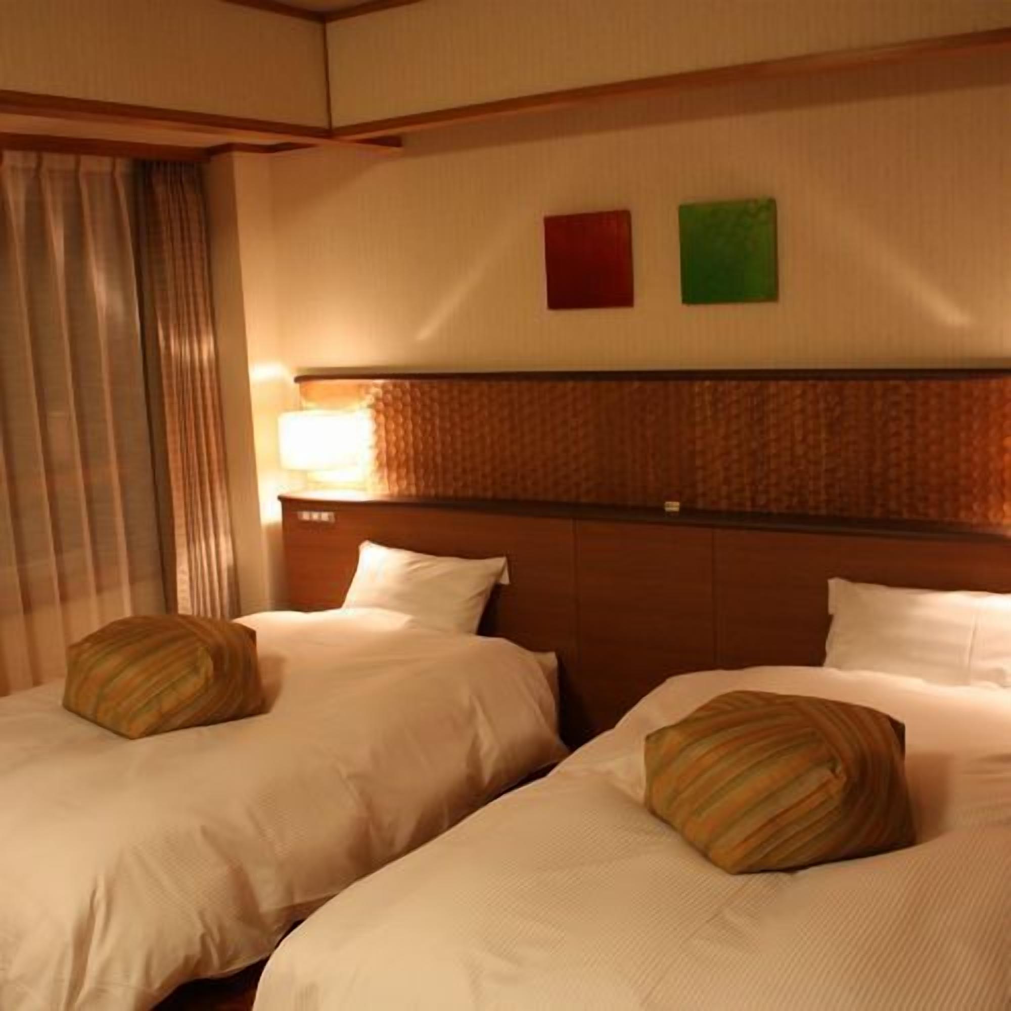 A hotel room with two beds, a headboard, a window with curtains, and a wall with two colored panels.