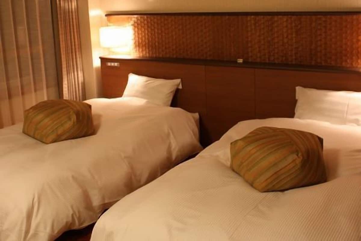 Habitación de hotel con dos camas, un cabecero, una ventana con cortinas y una pared con dos paneles de colores.