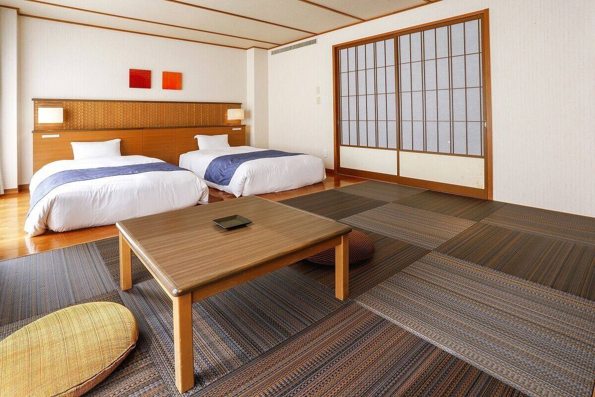 Habitación de hotel con dos camas, una mesa de madera, esteras de tatami y una puerta corredera de shoji.