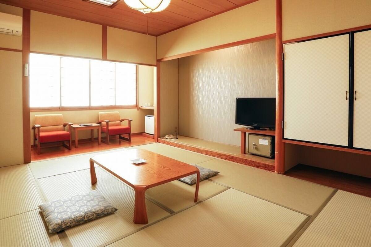 Una habitación japonesa tradicional con suelo de tatami, una mesita baja, un televisor y un armario.