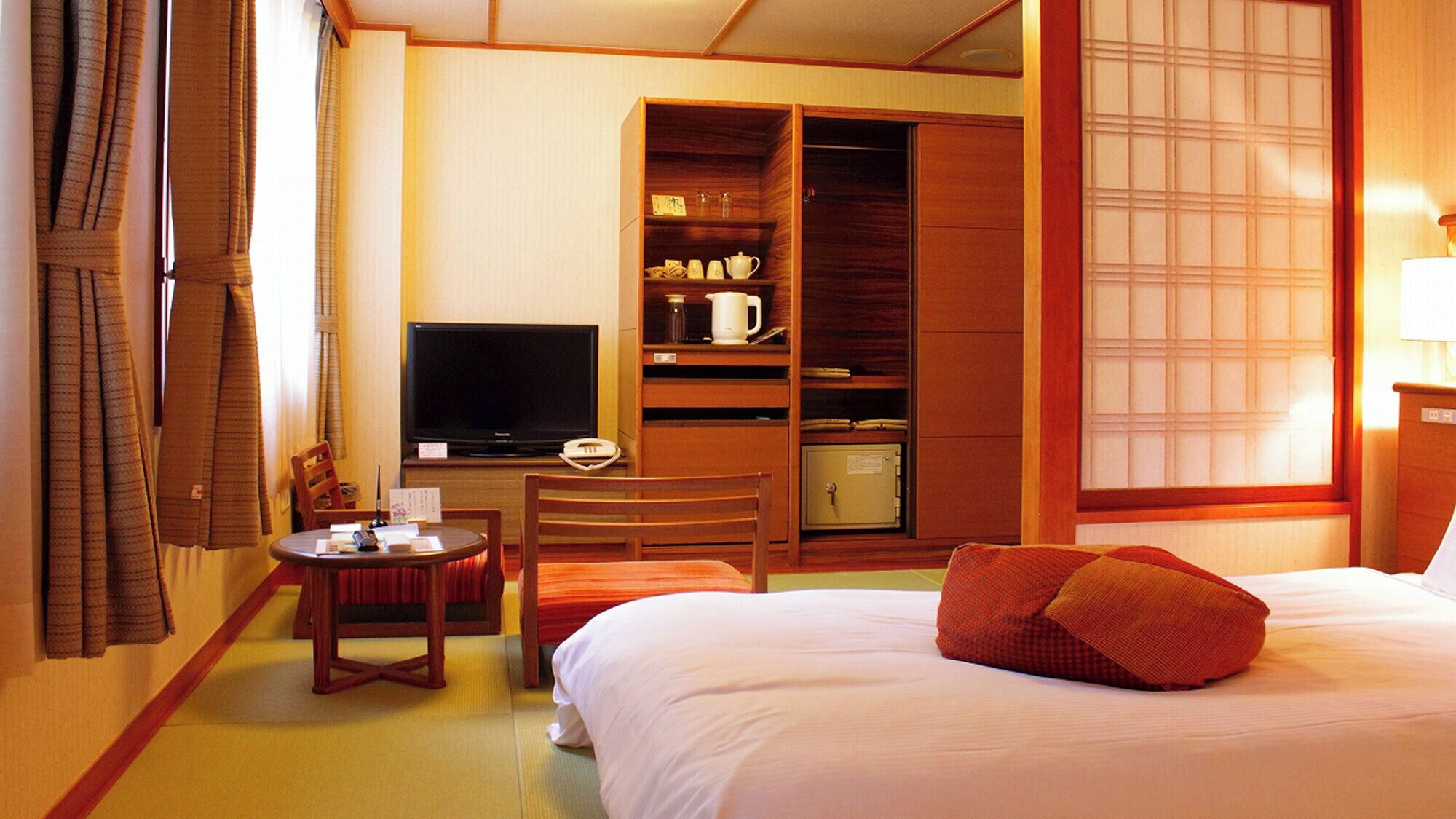 A hotel room with a bed, a television, a desk with a chair, a wardrobe, and a window with a view.