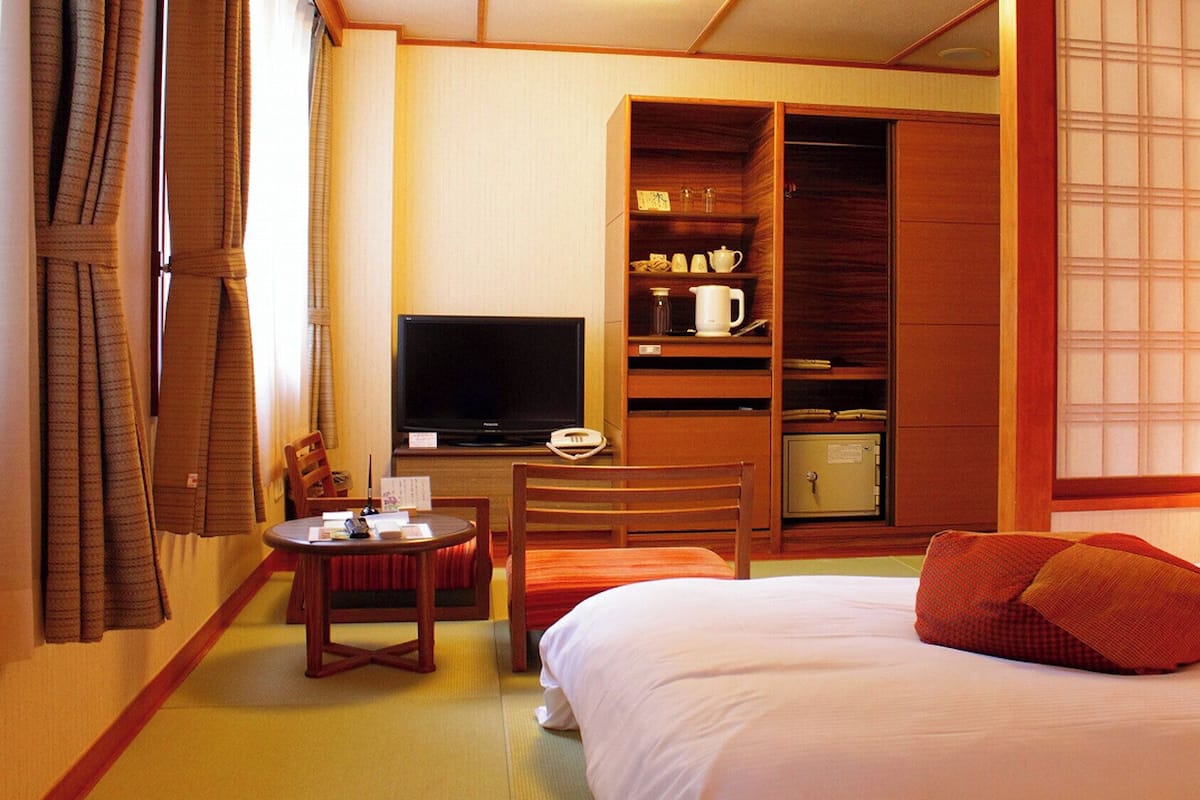 Habitación de hotel con cama, televisión, escritorio con silla, armario y ventana con vistas.