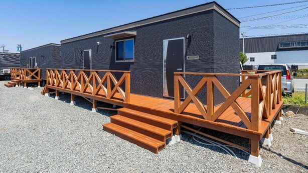 A modern building with a dark exterior, a wooden deck, and a small window. - KM Hotels North (Ozu)