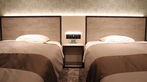 Quarto de hotel com duas camas, mesa de cabeceira com relógio e parede texturizada.