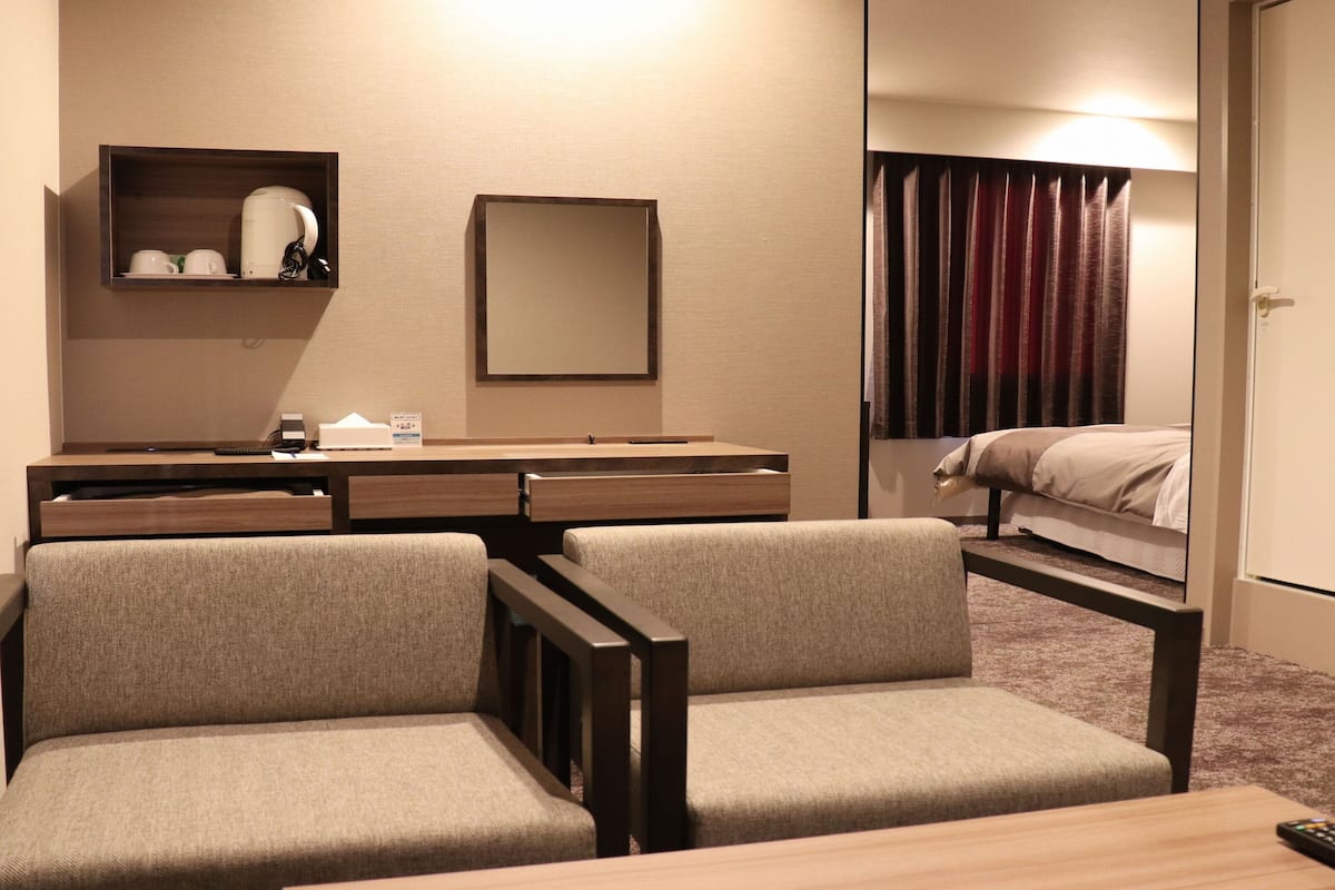 A hotel room with a desk, two chairs, a bed, a mirror, and a window with curtains.