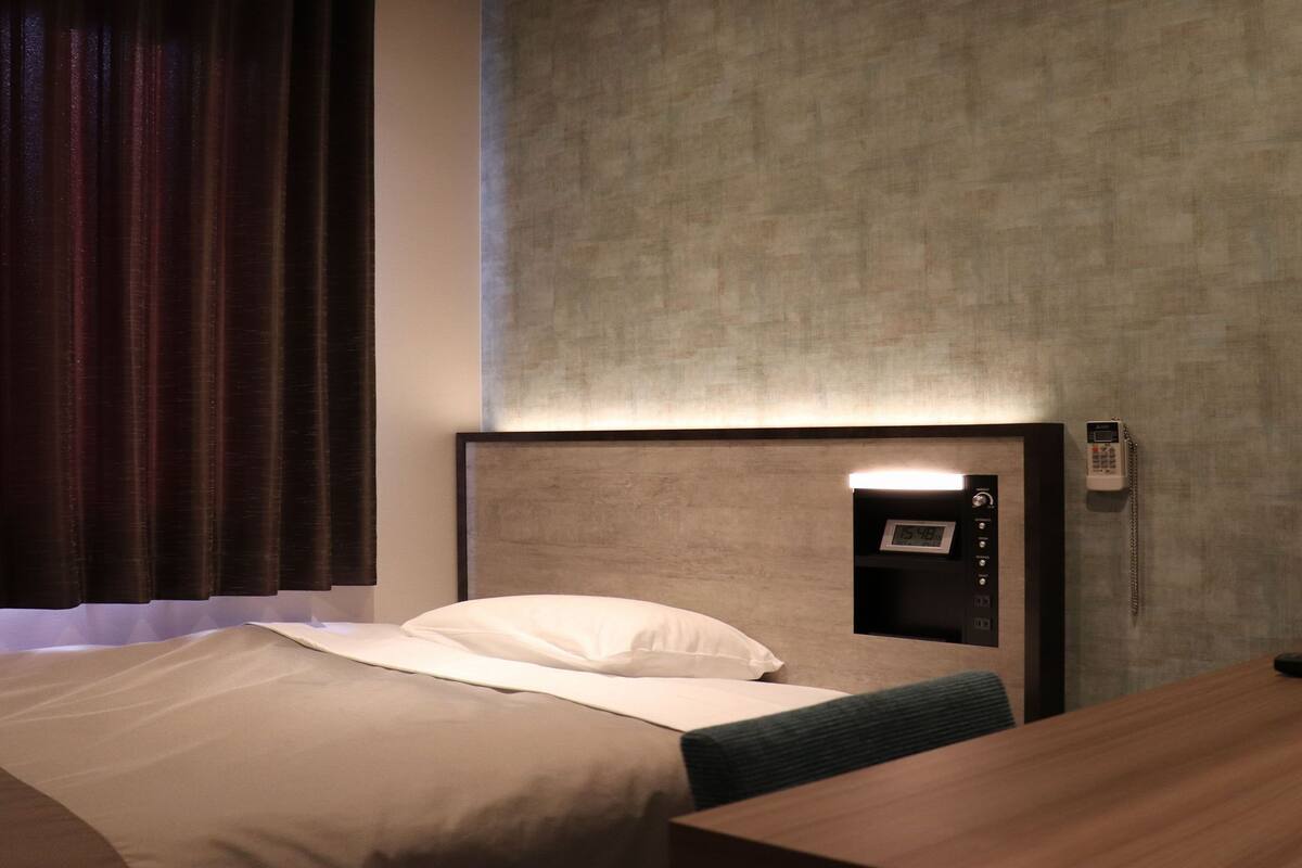 A hotel room with a bed, bedside table, and a wall-mounted phone.