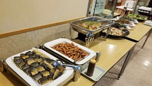 Buffet variado com diversos pratos, incluindo peixe, salsichas e saladas.