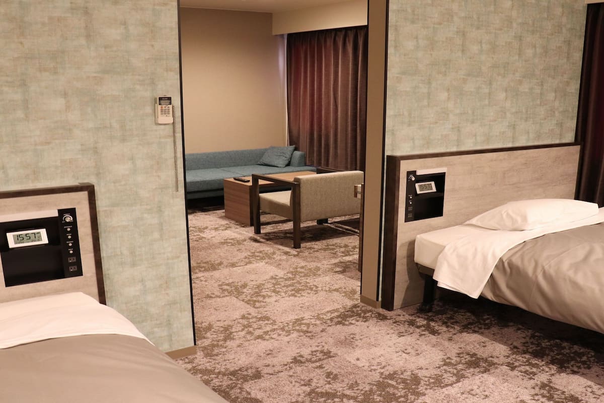 A hotel room with a bed, a desk, a chair, a sofa, and a clock on the wall.