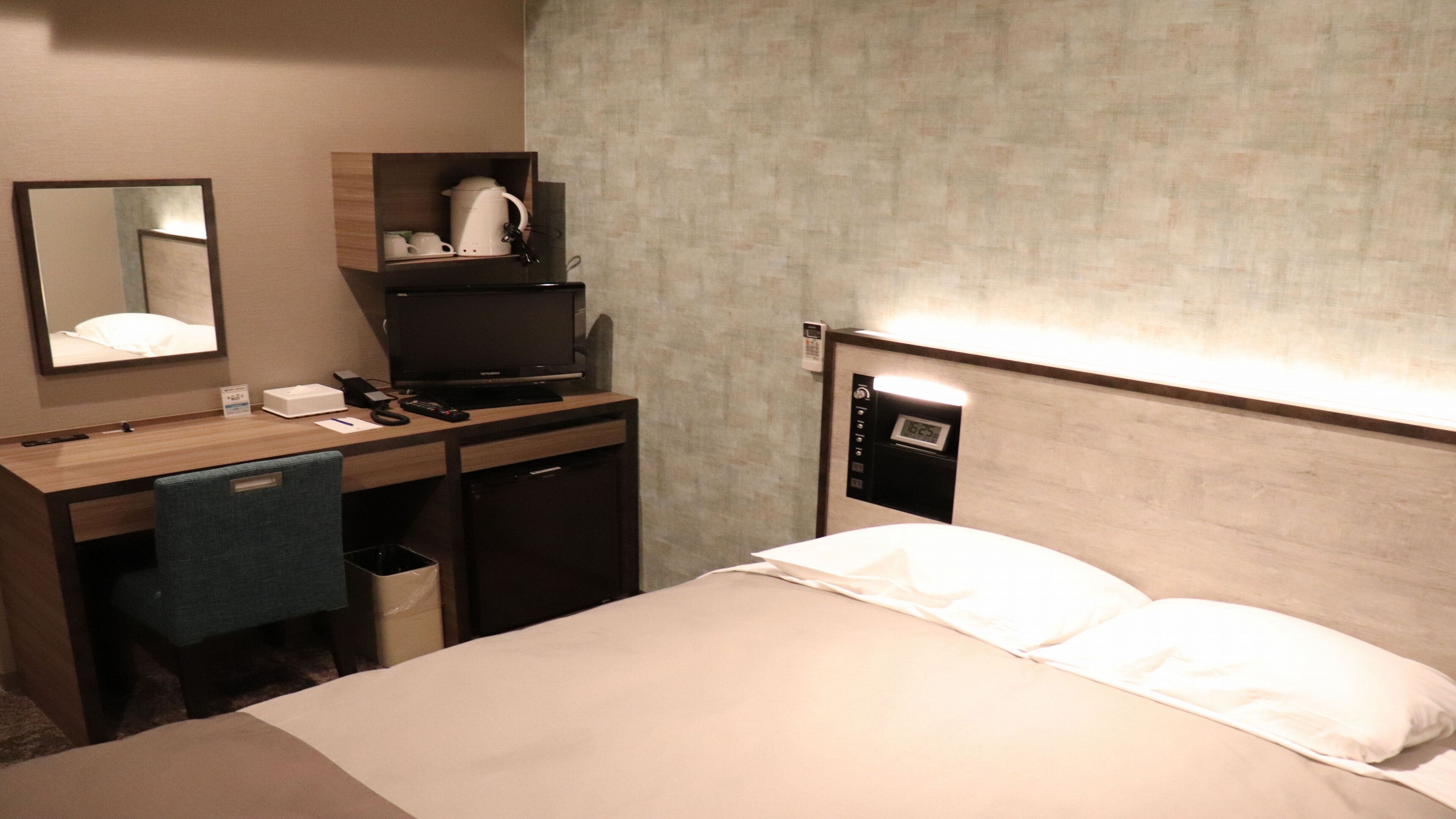 A hotel room with a bed, a desk with a computer, a mirror, a coffee maker, and a phone.