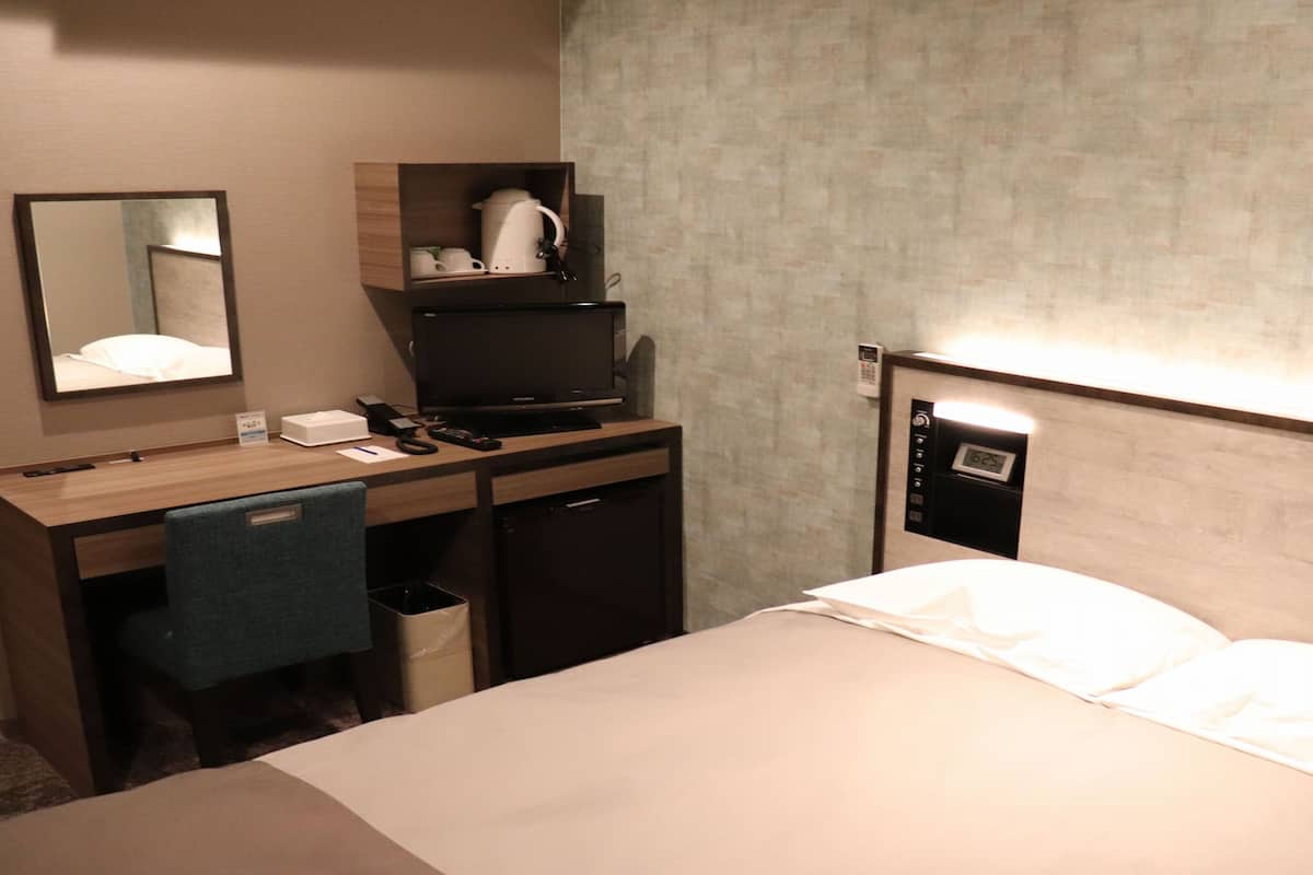 A hotel room with a bed, a desk with a computer, a mirror, a coffee maker, and a phone.