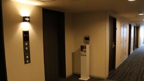 Corredor de hotel com elevador, balcão de recepção e portas de acesso aos quartos.