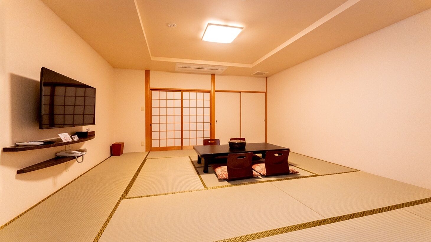 Perinteinen japanilaistyylinen huone, jossa on tatamimatto, matala pöytä tyynyineen, seinälle asennettu televisio ja liukuvat ovet.