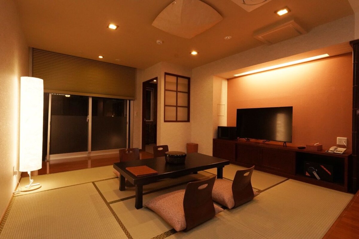 A room with a tatami mat floor, a low table, chairs, a television, and a sliding door.