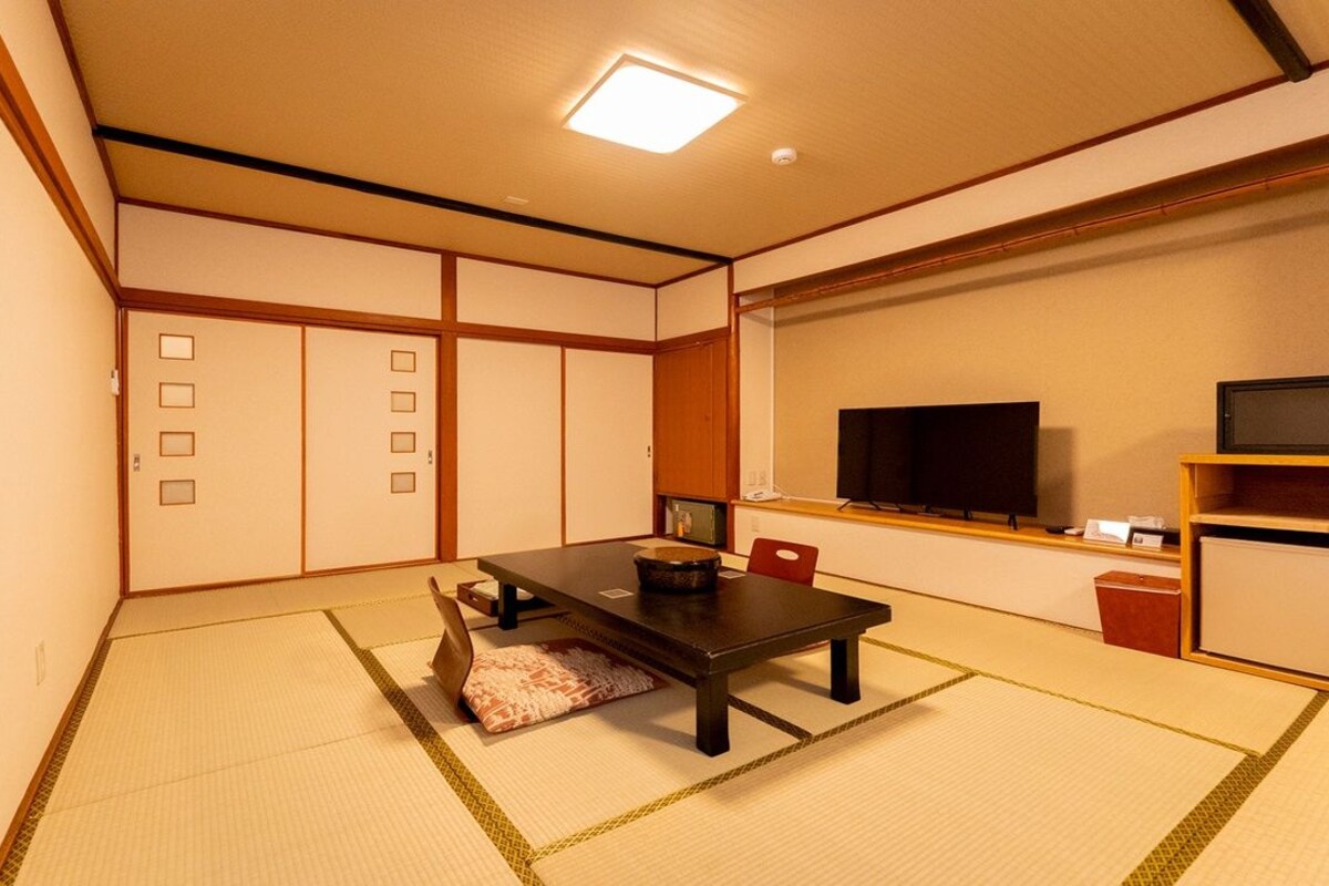 Een traditionele Japanse kamer met tatami vloerbedekking, een lage tafel, een televisie en een klein schap.