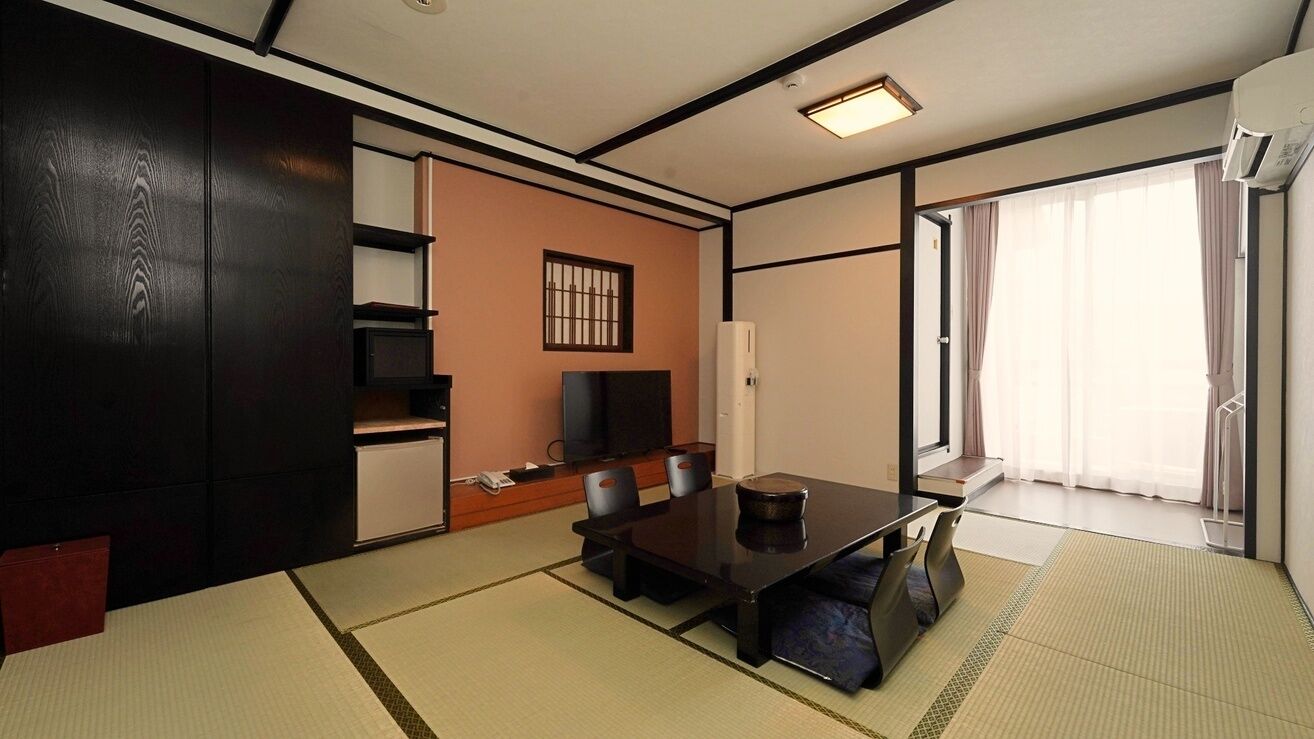 Perinteinen japanilaistyylinen huone, jossa on tatamimatto, matala pöytä tyynyineen, televisio ja liukuovi, joka johtaa parvekkeelle.