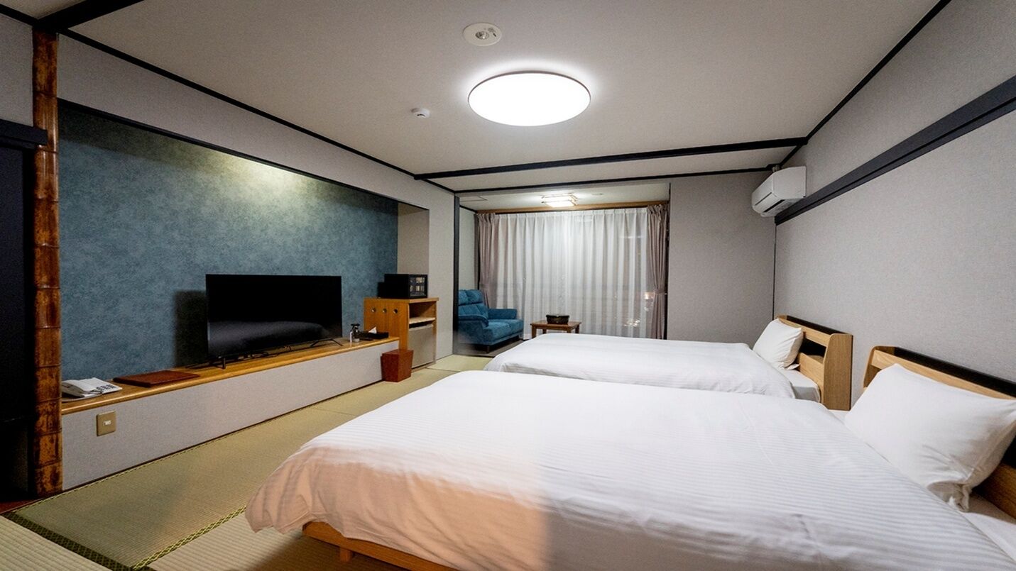 Ett hotellrum med två sängar, en TV, ett skrivbord och ett fönster med gardiner.